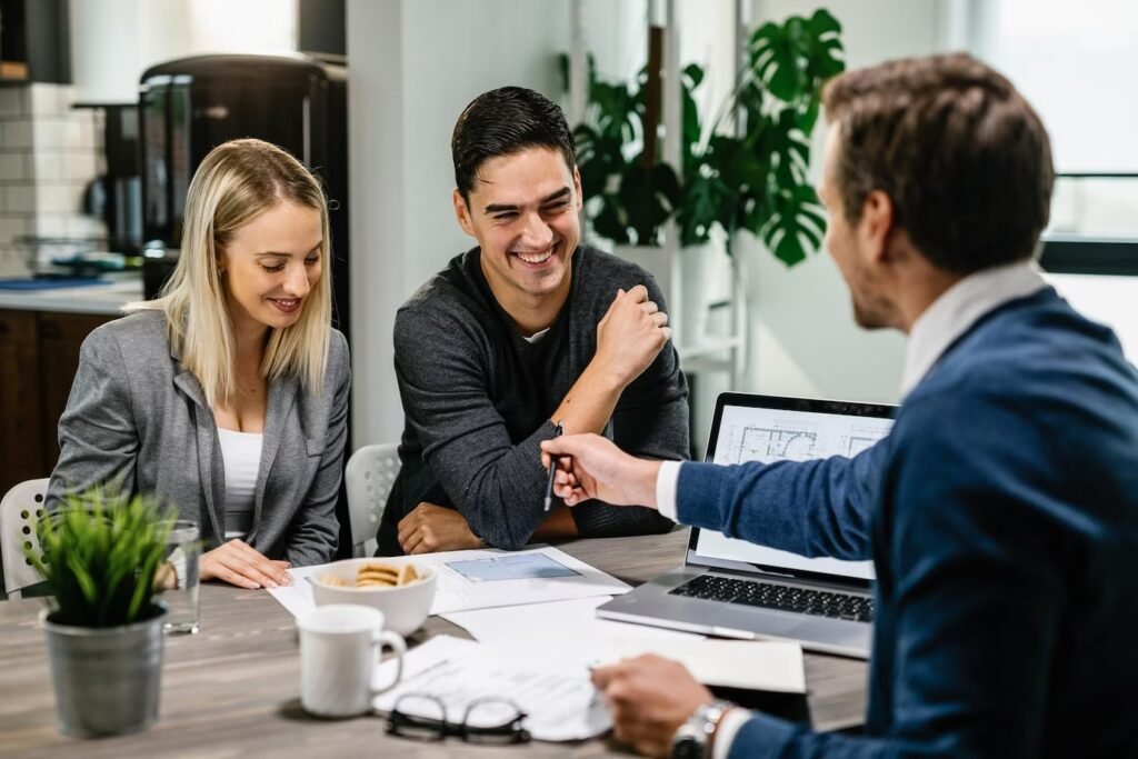 Happy couple meeting with a real estate agent, analyzing blueprints and discussing their plans.